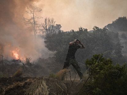 TOPSHOT - A man reacts as a helicopter sprays water at a fire in Gennadi, on the southern part of the Greek island of Rhodes on July 25, 2023, on July 25, 2023, during a wildfire. Wildfires have been raging in Greece amid scorching temperatures, forcing mass evacuations in several tourist spots including on the islands of Rhodes and Corfu. (Photo by Spyros BAKALIS / AFP)