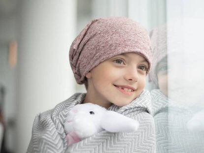 Una niña con cáncer mira por la ventana.