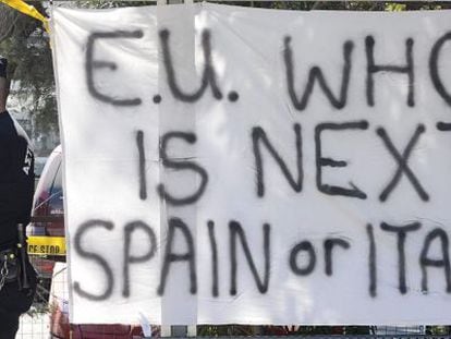 Un agente de la policía en Chipre junto a una pancarta que dice: “¿UE, quién es el próximo? España o Italia”.