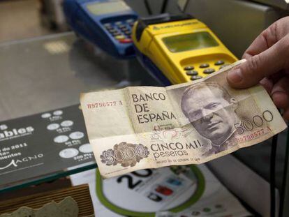 Un comerciante sostiene un billete de 5000 pesetas. 