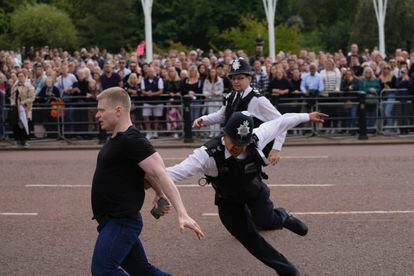 Agentes de policía persiguen a un hombre que salta una barrera momentos antes de la llegada de coche de Carlos III  al Palacio de Buckingham. 