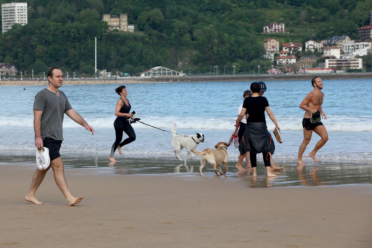 Diverse persone camminano e corrono con i cani sulla spiaggia di La Concha il 2 maggio.