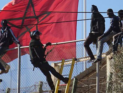 Un agente de la Guardia Civil intenta que los inmigrantes bajen de la valla.