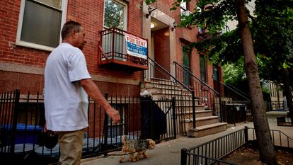 Un hombre pasea a su perro en el East Village de Nueva York junto a un cartel de se alquila piso.