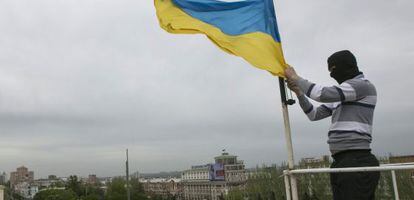 Un activista prorruso arr&iacute;a una bandera ucrania en un edificio oficial en Donetsk.
