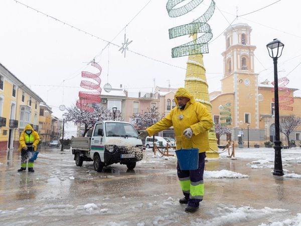 Dos trabajadores del ayuntamiento de Bullas esparcen sal para evitar que la nieve se convierta en hielo, este jueves, en la plaza del Ayuntamiento de Bullas (Murcia).