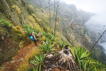 Santo Antao island at Cape Verde.  Female traveler staying on the cove volcano edge above the foggy green valley overgrown with agave plants.