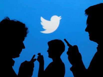 Tres personas consultan su teléfono móvil ante una pantalla de Twitter.