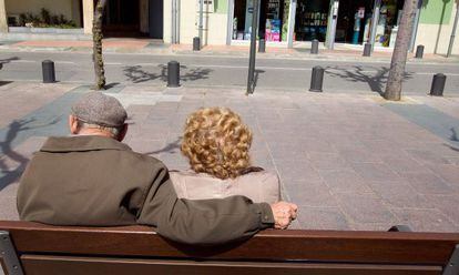 Una pareja de ancianos toma el sol en un banco.