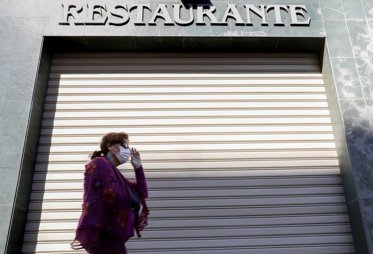 Una persona con mascarilla pasa delante de un restaurantes cerrado en Valencia.