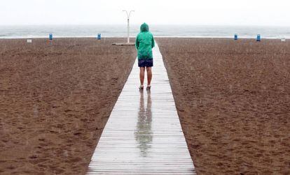 Una mujer contempla la playa de la Malvarrosa bajo la lluvia durante la mañana del domingo.