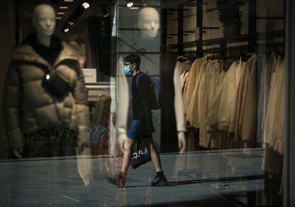 Un joven camina con mascarilla frente al escaparate de una tienda en Barcelona.