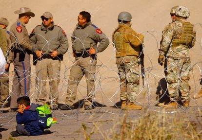 Un niño migrante, que viaja con su familia en busca de asilo, espera cerca de miembros de la Guardia Nacional de Texas.