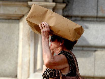 Una mujer se cubre la cabeza con una bolsa debido al fuerte sol en una ola de calor en Madrid.