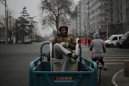 Un ciudadano chino permanece sentado en una silla a bordo de un motocarro en Pekín (China).