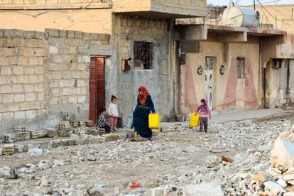 Una mujer y un niño llevan varias garrafas de agua por una calles del barrio de Gewayran, a las afueras de la ciudad de Al Hasaka, noreste de Siria. Decenas de excombatientes del Estado Islámico (ISIS, por sus siglas en inglés) huyeron de la vecina cárcel de Al Sina tras un ataque yihadista que pretendía liberarlos y las milicias kurdas y los extremistas se enfrentaron durante 10 días en este distrito, donde las huellas de la violencia son aún flagrantes. Ningún vecino ha recibido indemnización para reconstruir su casa y todos temen un nuevo ataque.