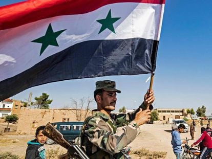 Un soldado del régimen ondea este lunes una bandera de Siria en la entrada occidental de Tal Tamr tras la entrada de las tropas regulares en esta localidad del norte sirio.