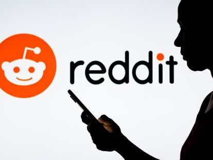 Una mujer sostiene un teléfono inteligente con el logotipo de Reddit en el fondo.