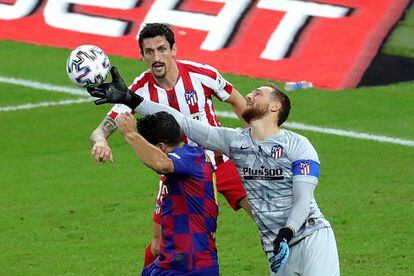 El portero esloveno del Atlético de Madrid, Jan Oblak, despeja el balón ante el delantero uruguayo del FC Barcelona Luis Suárez, en presencia del defensa montenegrino Stefan Savic.