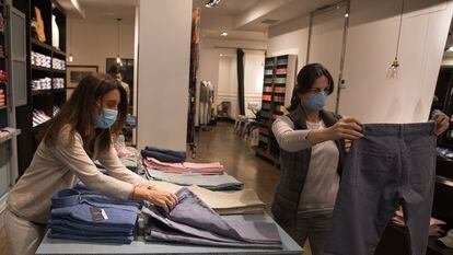 La propietaria (izquierda) y una clienta, ambas con mascarilla, miran ropa de hombre en Lester, una tienda de moda de Madrid que ha reabierto este lunes.