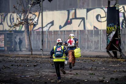 Dos voluntarios corren para protegerse en medio de una protesta en Santiago.