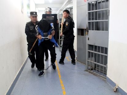 Un recluso de un centro de reeducación del condado de Tekes, en Xinjiang, encapuchado, con esposas y grilletes en los pies, es trasladado por agentes en septiembre de 2018.