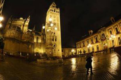 Una mujer se protege de la lluvia registrada hoy en Sevilla, a su paso por la plaza de la Virgen de los Reyes, desde donde procesionarían diversas hermandades que finalmente no lo han podido llevar a cabo por la lluvia.