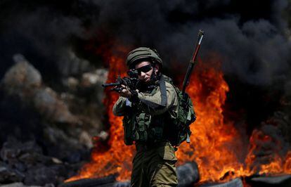 Un soldado israelí camina apuntando con su arma a palestinos que se manifiestan en la localidad de Kofr Qadom, cerca de Nablus (Palestina).