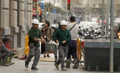 Dos trabajadores echan escombros en un contenedor en una calle de Barcelona.