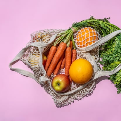 Reusable cotton mesh bag with fruit and vegetables on pink background. Zero Waste shopping concept.