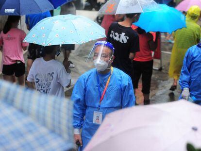 Un trabajador sanitario pasa ante una fila de residentes y turistas, este lunes en la ciudad china de Sanya.