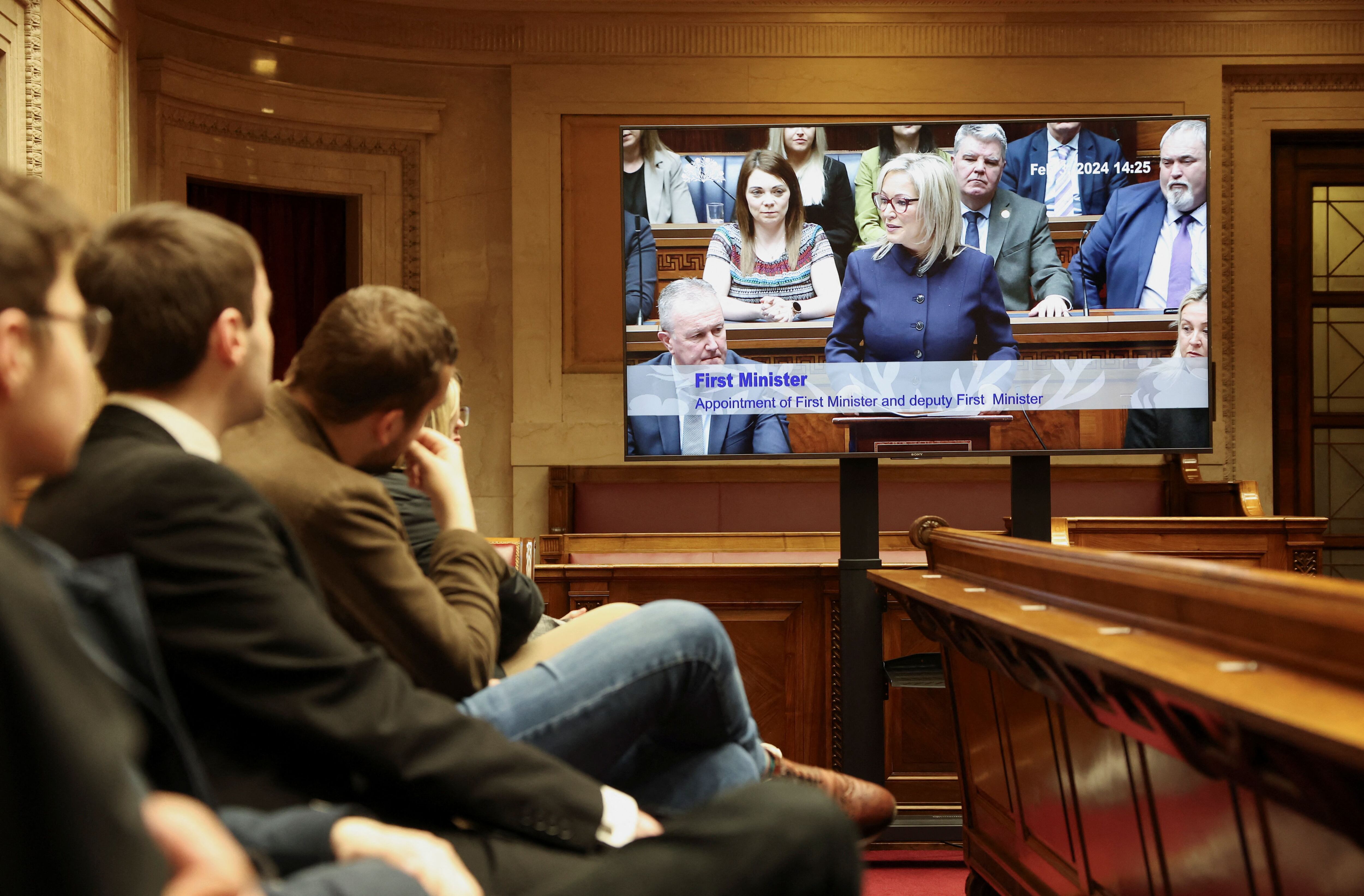 Visitantes y miembros de la prensa observan a Michelle O’Neill pronunciar su discurso de aceptación en una sala de los edificios del Parlamento de Stormont, este sábado en Belfast.