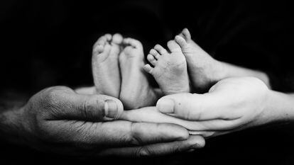 Dos padres sujetan los pies de sus bebés mellizos.
