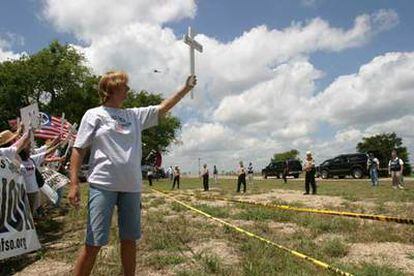 Cindy Sheehan muestra una cruz con el nombre de su hijo muerto en Irak al paso de la caravana del presidente Bush en Crawford.