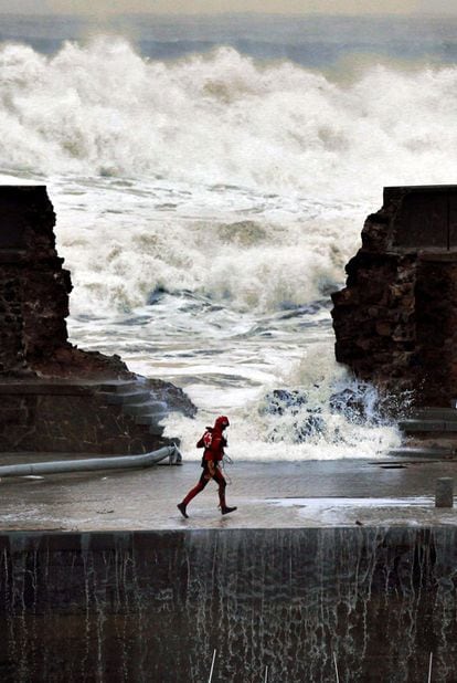 Un miembro de la Cruz Roja del Mar pasa ante la brecha originada en el rompeolas del puerto de Bermeo.