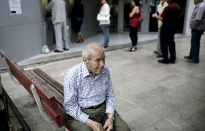 Un pensionista, sentado ante una cola en un cajero.