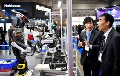 Un par de asistentes observan un robot industrial en una feria de rob&oacute;tica en Tokio. 