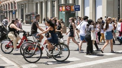 Gente en bicicleta y a pie cruza una calle en la Plaza de Cataluña.
