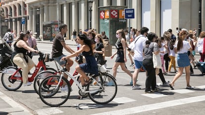 Gente en bicicleta y a pie cruza una calle en la Plaza de Cataluña.