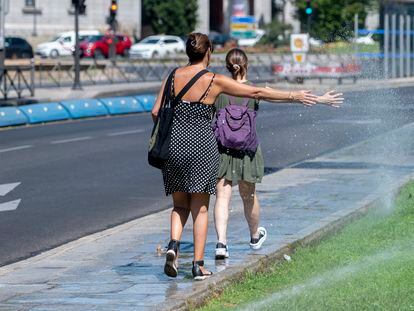 Dos mujeres se mojan con unos chorros de aspersores, a 21 de agosto de 2023, en Madrid.