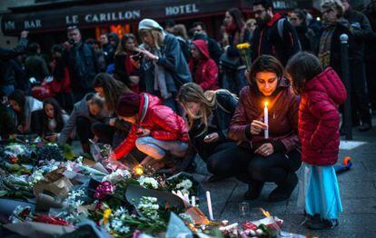 Distintas personas dejan flores y velas en recuerdo de las v&iacute;ctimas de Par&iacute;s frente al restaurante Le Carillon.