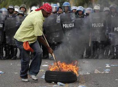 Un seguidor de Zelaya manipula un neumático ardiendo ante una formación de policías antidisturbios, durante la protesta del martes en Tegucigalpa.