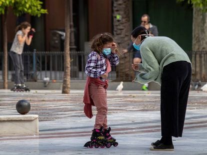 Una niña en patines y con mascarilla conversa con una mujer esta tarde en la Plaza Nueva de Sevilla.
