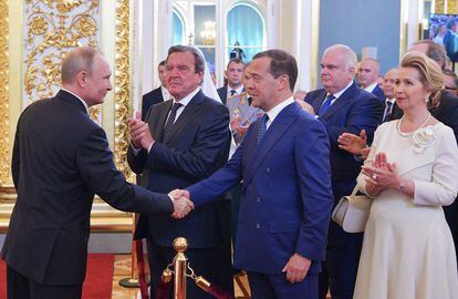 Vladimir Putin (izquierda) estrecha la mano del primer ministro ruso, Dmitry Medvedev (centro), mientras la esposa de este último, Svetlana Medvedeva (derecha) y el excanciller alemán Gerhard Schröder (segundo por la izquierda), aplauden, durante la sesión de investidura del máximo mandatario ruso, en el Gran Palacio del Kremlin.