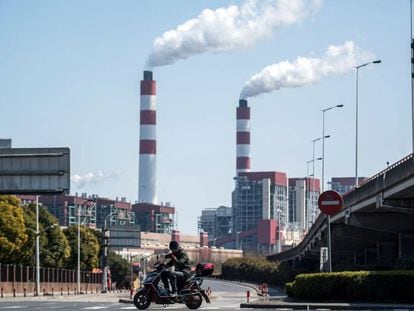 Un motociclista pasa frente a las chimeneas humeantes de una central de generación eléctrica en Shaghái (China).