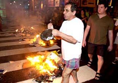 Participantes en una cacerolada de protesta en el centro de Buenos Aires pasan ante restos de basura quemada.