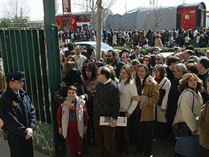 Una gran fila de personas se dirigen a votar en el barrio de El Pozo; al fondo, el tren en el que viajaban las víctimas del atentado.