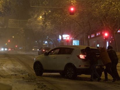 Varias personas empujan un coche atascado por la nieve en Madrid.