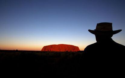Un hombre mira el monte Uluru al atardecer. 