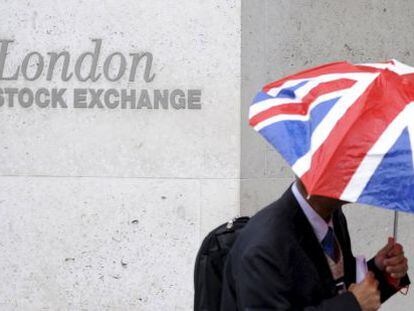 Un hombre con un paraguas con la bandera de Reino Unido pasa frente a la Bolsa de Londres.